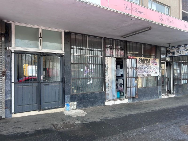 Commercial storefront featuring a tiled facade, security gates, and metal window grilles, located along a covered pedestrian walkway.