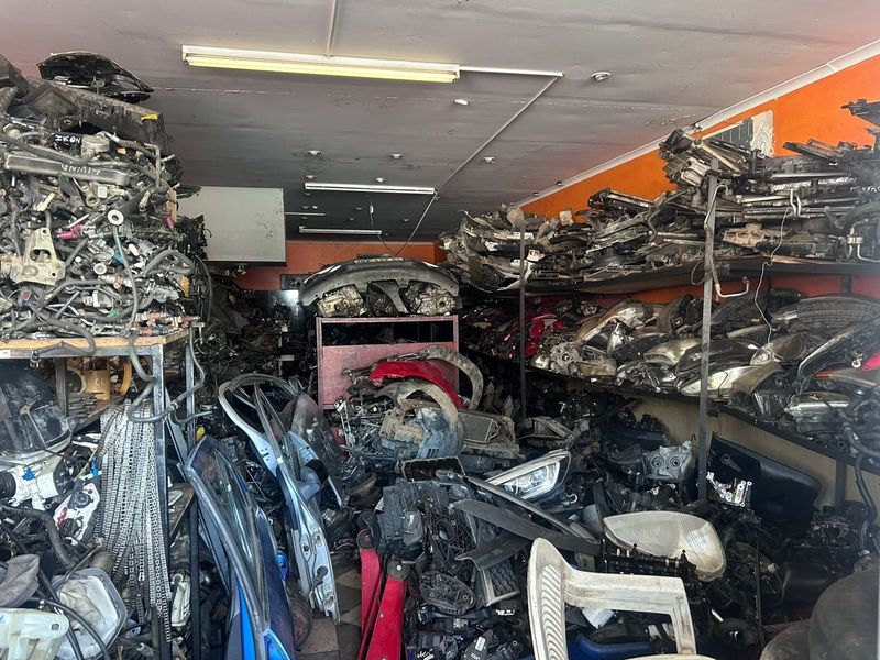 A commercial utility space or storage area currently utilized for automotive parts inventory, featuring industrial metal shelving and overhead fluorescent lighting.