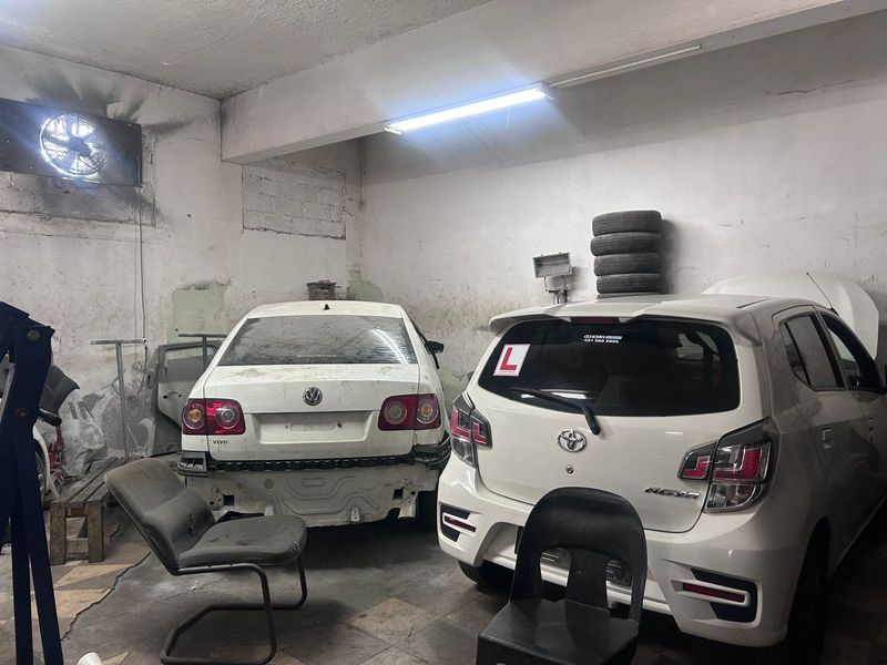 A commercial garage space featuring industrial ventilation, fluorescent lighting, and concrete flooring, currently showing significant wear to the wall finishes.
