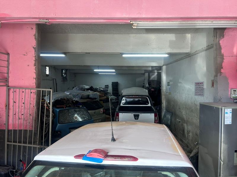 A commercial garage space featuring concrete structural elements, fluorescent lighting, and a metal security gate entrance.