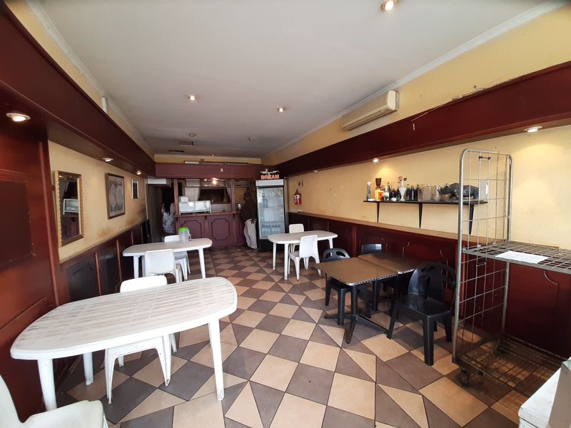 Open-plan commercial dining area featuring tiled flooring, wall-mounted air conditioning, and built-in wooden paneling, suitable for a restaurant or cafe layout.