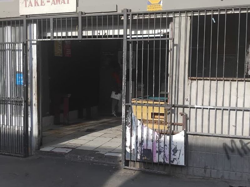 Street-level commercial storefront featuring a security gate and bars, showing signs of wear and requiring maintenance to the facade and signage.