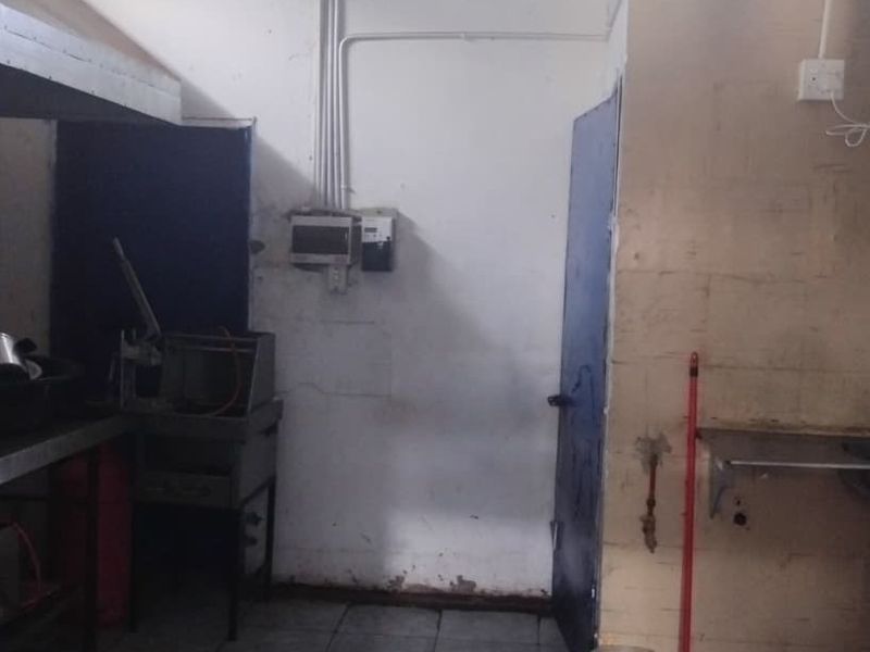 A functional scullery or utility area featuring a stainless steel sink, exposed plumbing and electrical services, and basic wall finishes requiring maintenance.