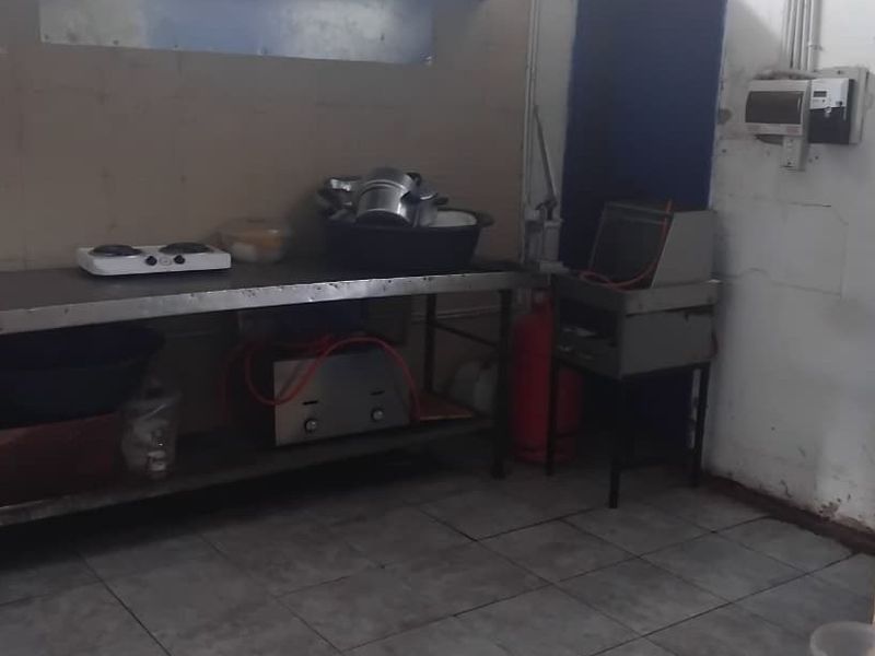 A functional kitchen area featuring tiled flooring and a stainless steel prep table, currently showing signs of wear and requiring maintenance.
