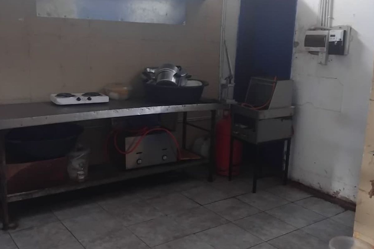 A functional kitchen area featuring tiled flooring and a stainless steel prep table, currently showing signs of wear and requiring maintenance.