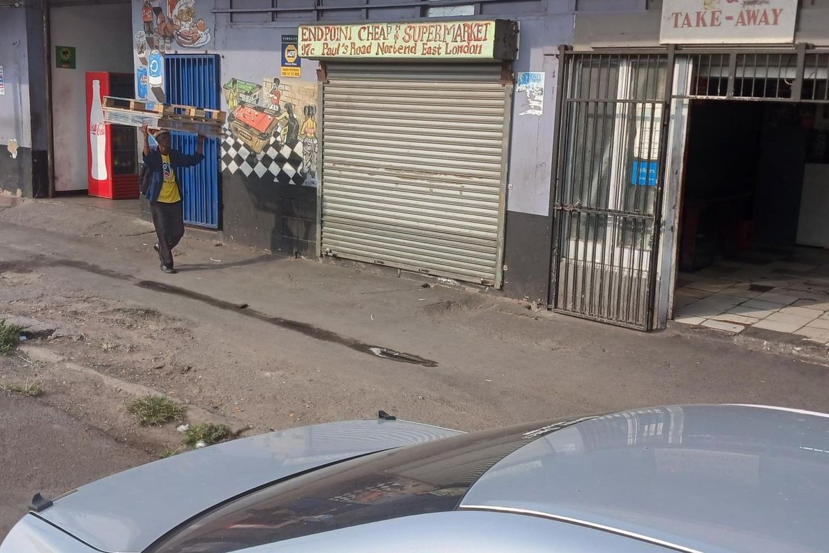 Street-level view of a commercial storefront featuring a security roller shutter and metal gate entrance in a high-traffic urban location.