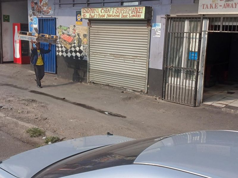 Street-level view of a commercial storefront featuring a security roller shutter and metal gate entrance in a high-traffic urban location.