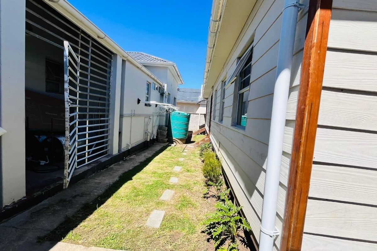 A narrow side passage between two building structures featuring weatherboard cladding, a water tank, and a small grassed area with paving stones.