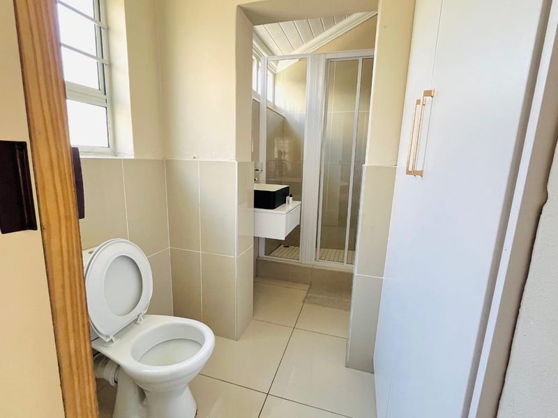 A functional bathroom featuring a toilet, a separate shower enclosure, and a wall-mounted vanity with neutral tiled finishes throughout.