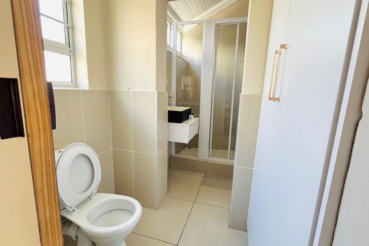 A functional bathroom featuring a toilet, a separate shower enclosure, and a wall-mounted vanity with neutral tiled finishes throughout.