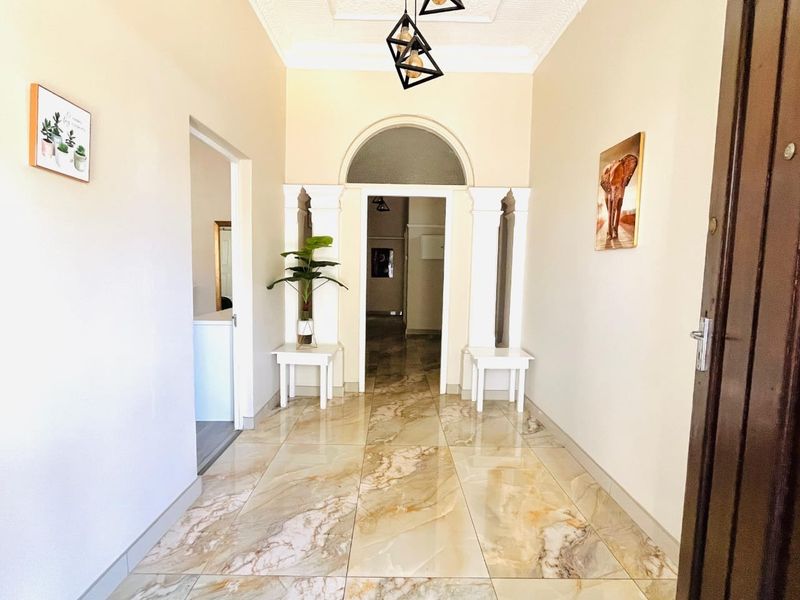 A bright and welcoming entrance hall featuring polished marble-look floor tiles, an elegant arched doorway with decorative columns, and ornate ceiling detailing.