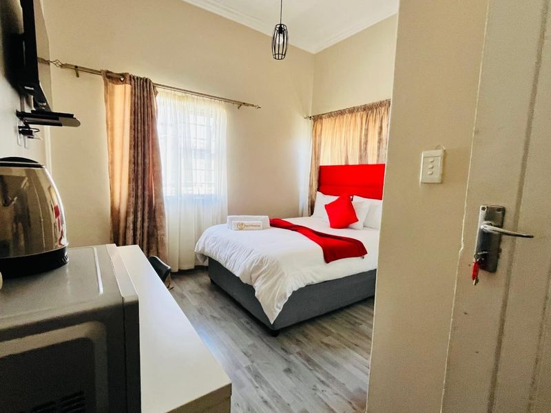 A well-maintained guest bedroom featuring laminate flooring, neutral wall tones, and dual windows with curtain rods, providing a comfortable and functional space.