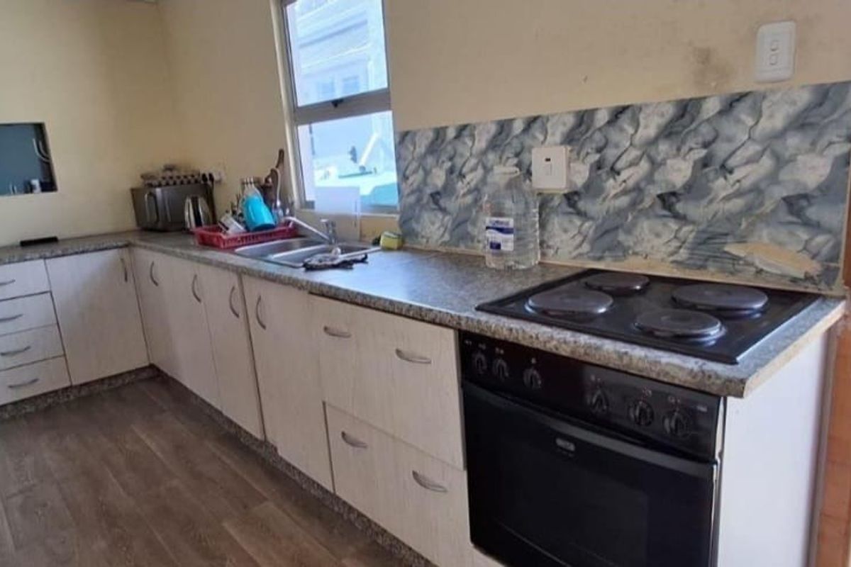 A functional kitchen featuring built-in cabinetry, laminate countertops, a stainless steel sink, and an integrated electric oven and hob with a tiled backsplash.