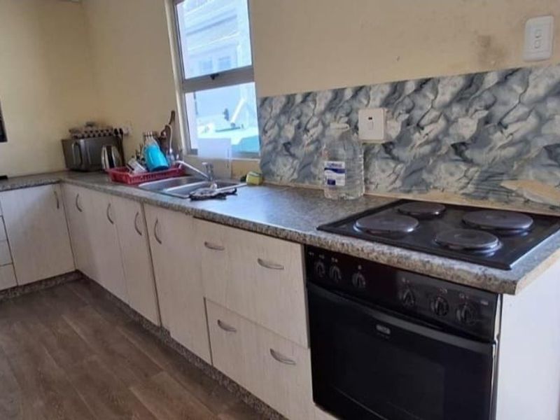A functional kitchen featuring built-in cabinetry, laminate countertops, a stainless steel sink, and an integrated electric oven and hob with a tiled backsplash.