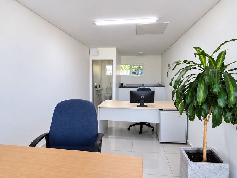 A clean, modern commercial office space featuring tiled flooring, integrated kitchenette cabinetry with a sink, and a private en-suite bathroom.