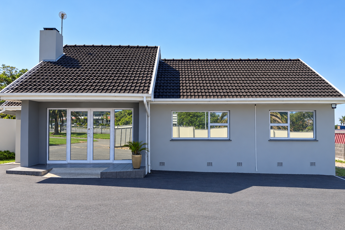 A well-maintained commercial building exterior featuring a dark tiled roof, grey rendered walls, aluminium windows, and a paved asphalt driveway.