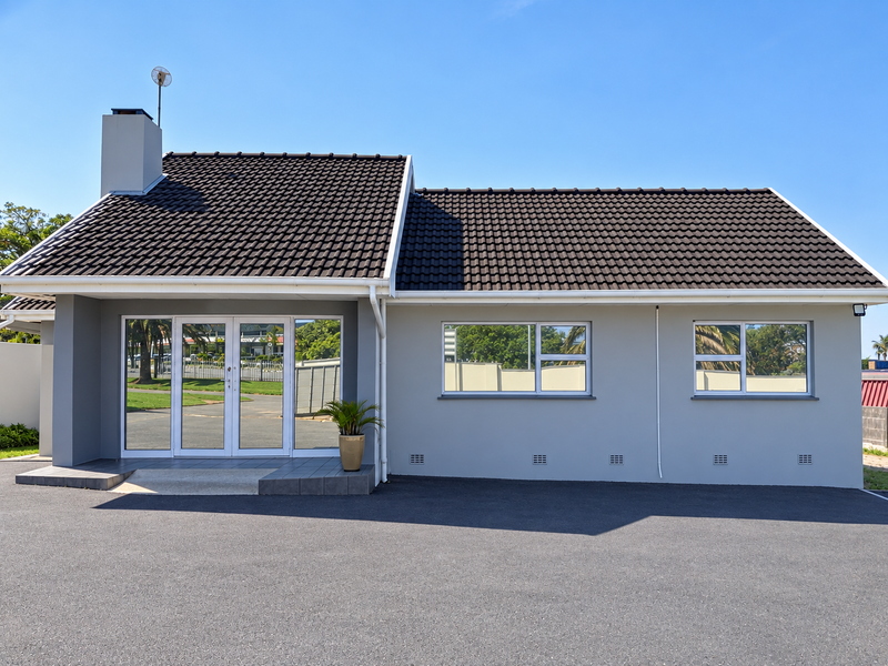 A well-maintained commercial building exterior featuring a dark tiled roof, grey rendered walls, aluminium windows, and a paved asphalt driveway.