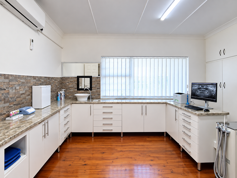 A well-maintained dental or medical office featuring extensive built-in cabinetry, stone-look countertops, a vessel sink, and polished timber flooring.
