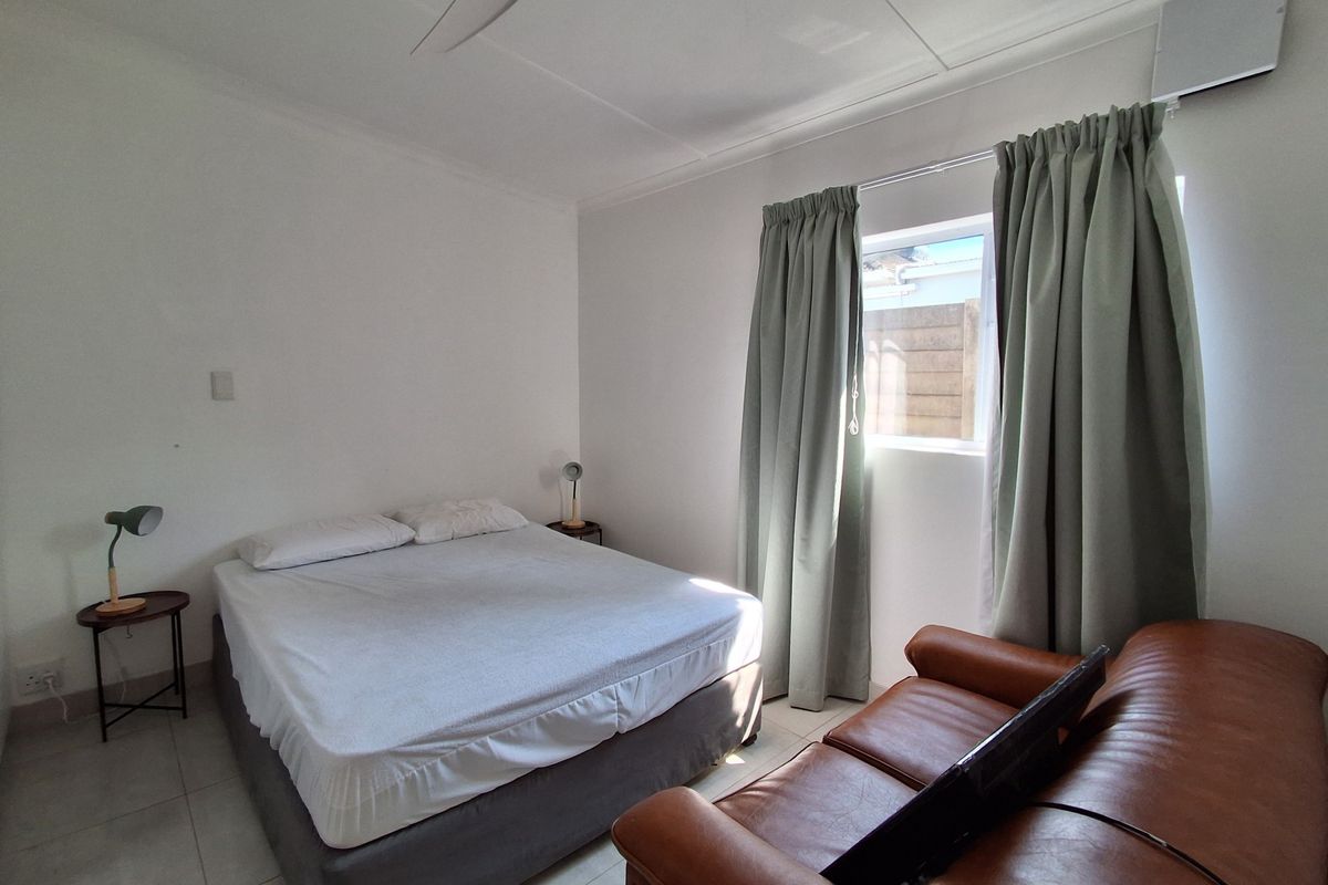A clean and functional bedroom featuring tiled flooring, a ceiling fan, and neutral wall finishes with natural light from the window.