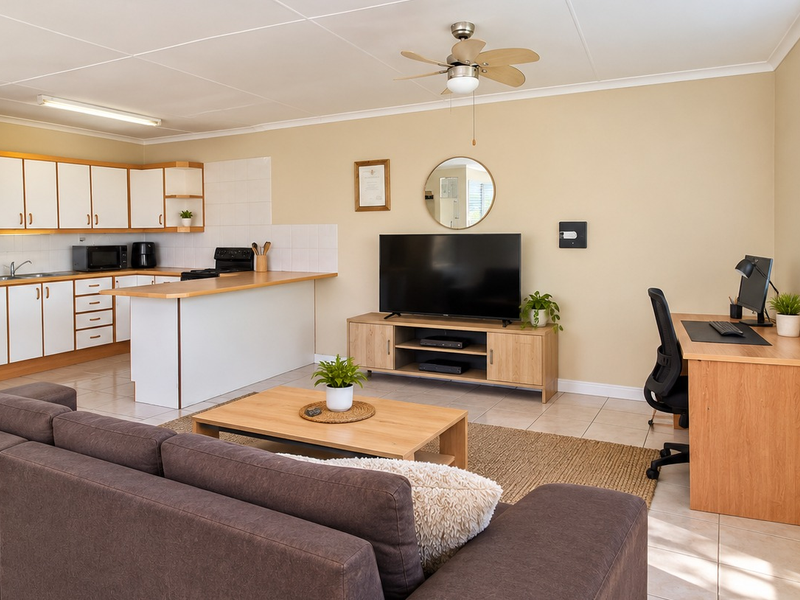 An open-plan office space featuring a functional kitchen area with built-in cabinetry, tiled flooring, and a ceiling fan, offering a versatile workspace layout.
