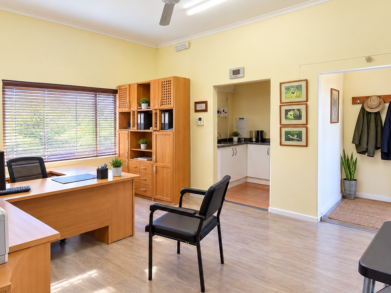 A well-maintained office space featuring laminate flooring, a ceiling fan, built-in storage cabinetry, and an adjoining kitchenette area.