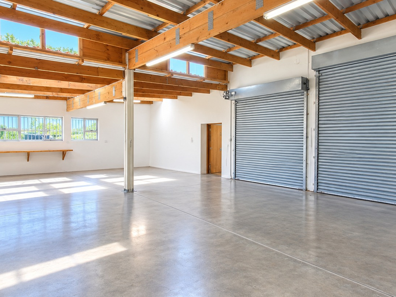 Spacious open-plan office or industrial workspace featuring polished concrete floors, exposed timber ceiling beams, and dual roller shutter doors for easy access.