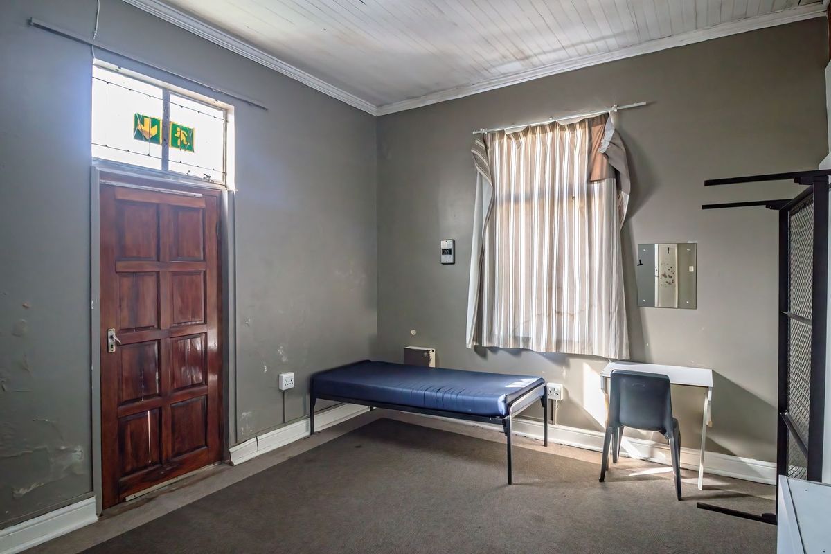 A bedroom featuring a timber door with a stained glass transom, neutral wall tones, and standard window treatments, requiring cosmetic updates to improve condition.