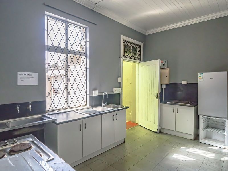 Functional commercial kitchen space featuring built-in cabinetry, stainless steel sink, electric hob, and security-barred windows with tiled flooring.