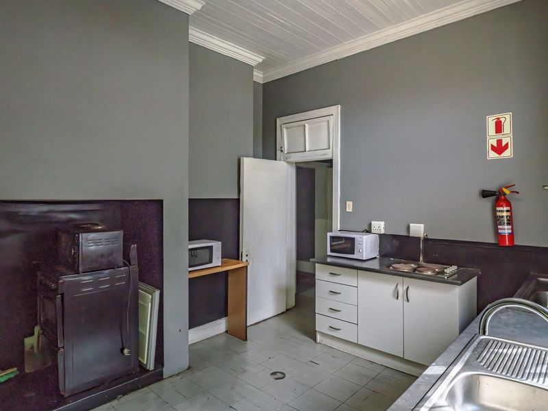 A functional commercial kitchen area featuring built-in cabinetry, stainless steel sinks, and essential fire safety equipment, with neutral grey wall finishes.