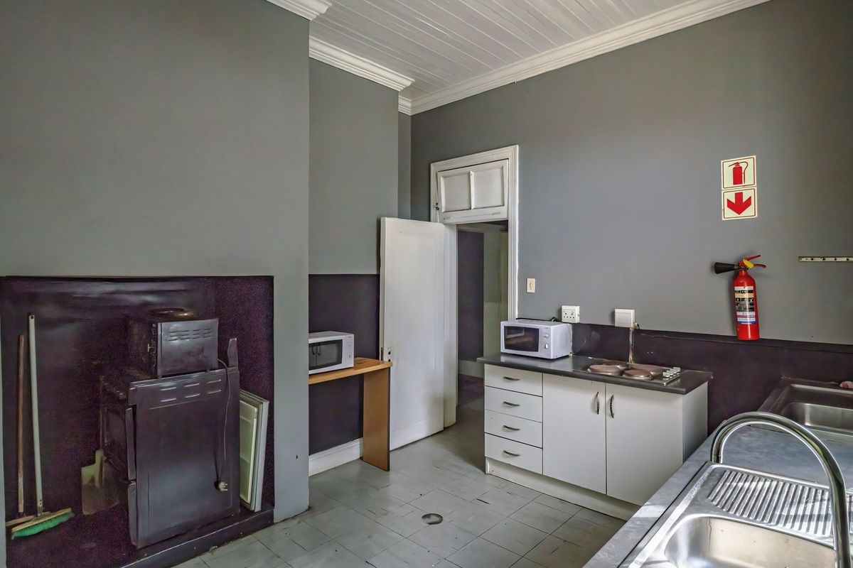 A functional commercial kitchen area featuring built-in cabinetry, stainless steel sinks, and essential fire safety equipment, with neutral grey wall finishes.