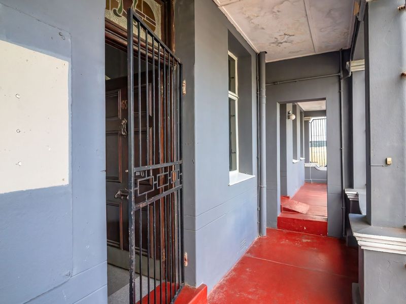 Covered front entrance porch featuring a security gate, timber door with stained glass detail, and painted concrete flooring.
