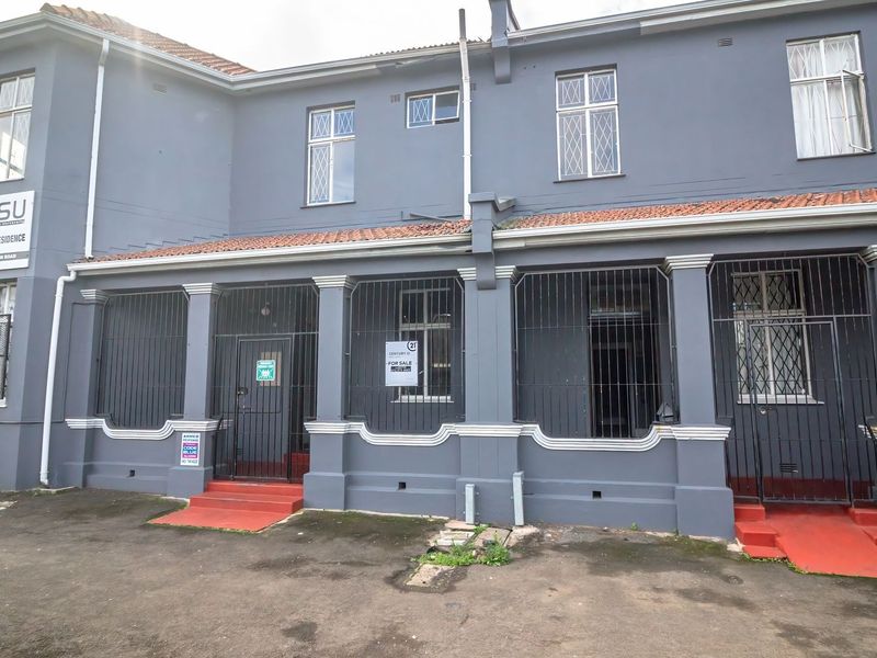 Front elevation of a commercial property featuring a grey plastered facade, tiled roof, and secure gated entrances with paved driveway access.