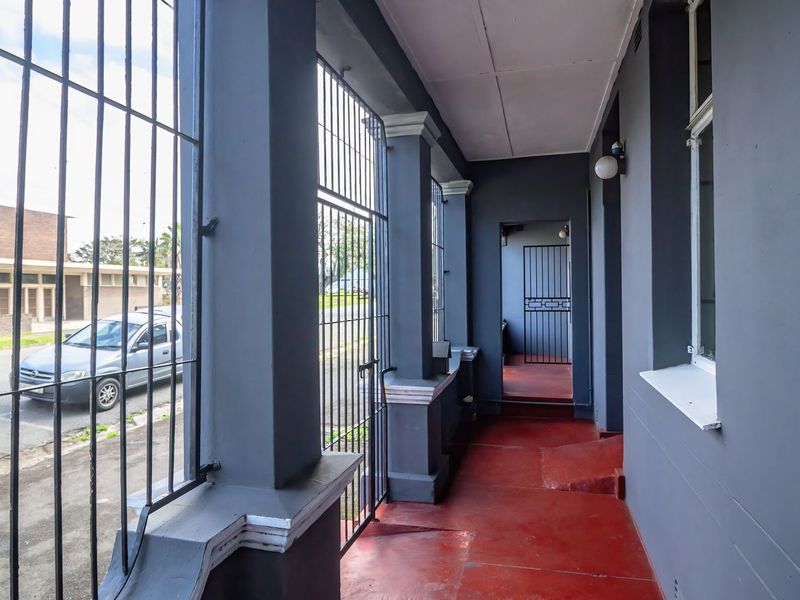 A covered exterior patio area featuring security bars, concrete pillars, and a painted floor, providing a secure entrance transition.