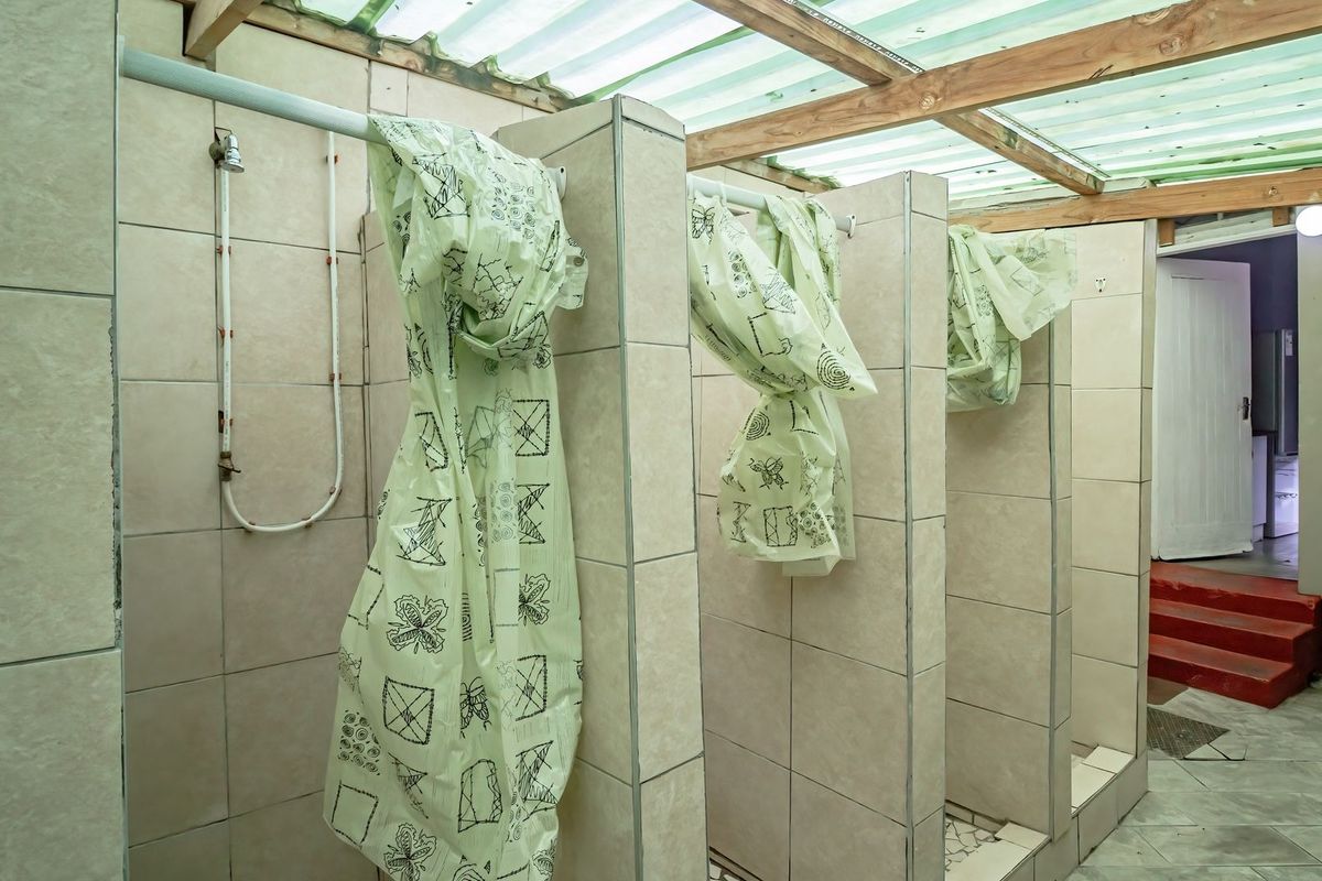 A communal bathroom area featuring multiple tiled shower cubicles with a translucent roof structure, providing functional utility space.