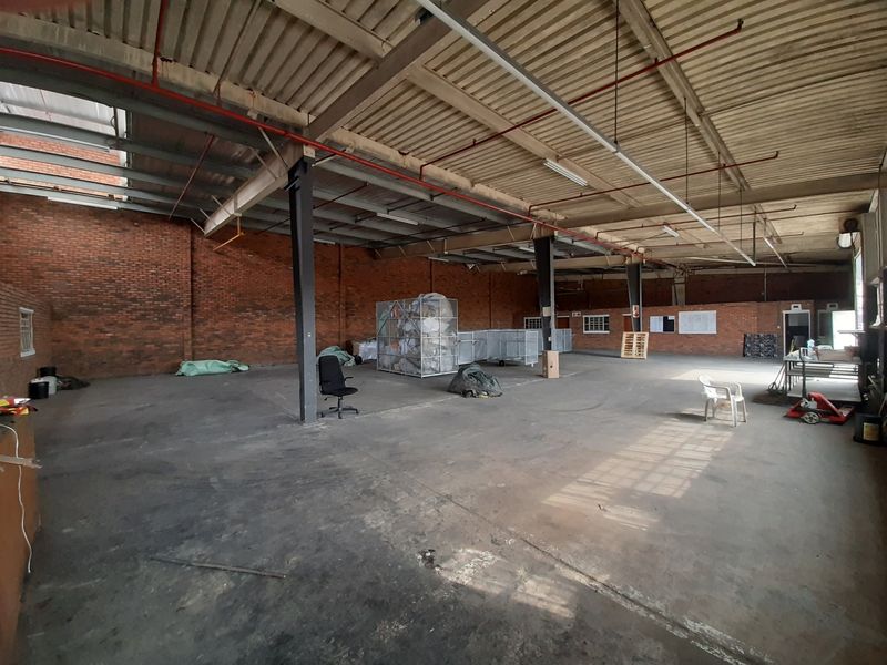 Spacious industrial warehouse unit featuring exposed brick walls, high ceilings with fire sprinkler systems, and durable concrete flooring.