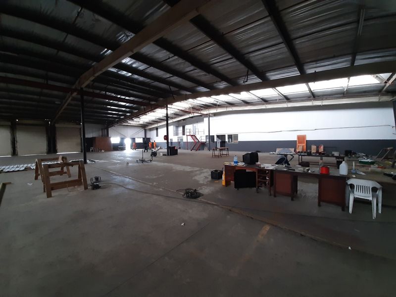 Spacious industrial warehouse featuring high ceilings with exposed steel trusses, skylights, concrete flooring, and a mezzanine level with metal staircase access.