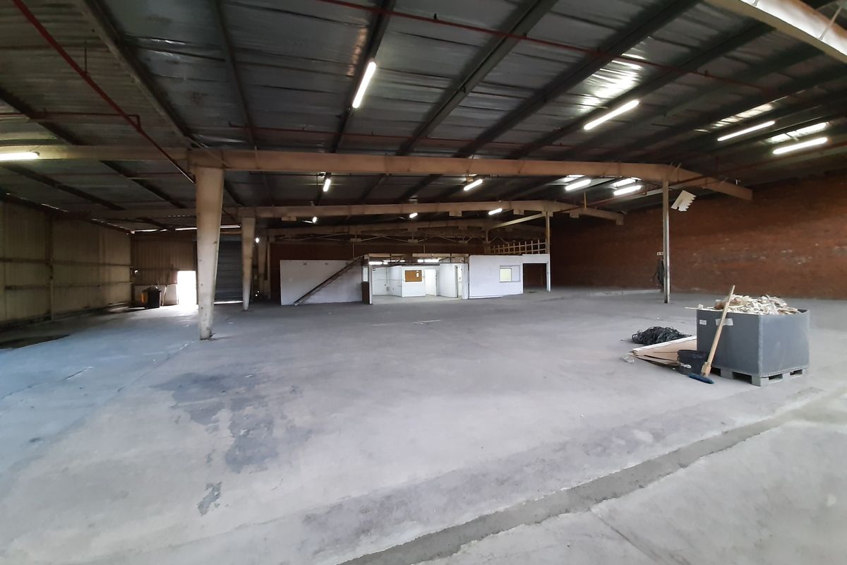 Spacious industrial warehouse featuring high ceilings with exposed steel trusses, concrete flooring, and an integrated mezzanine office area.