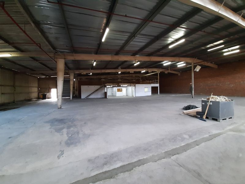 Spacious industrial warehouse featuring high ceilings with exposed steel trusses, concrete flooring, and an integrated mezzanine office area.