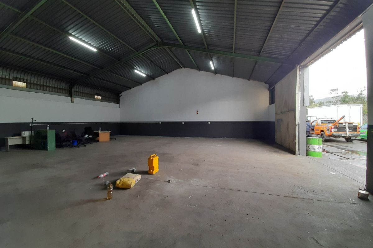 Spacious industrial warehouse or garage area featuring high ceilings, concrete flooring, and a large access door, suitable for storage or workshop use.