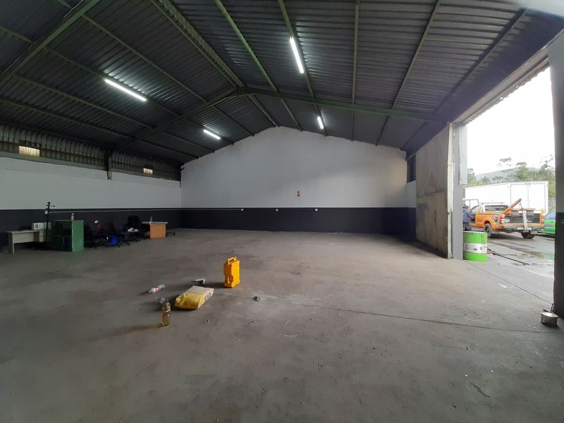 Spacious industrial warehouse or garage area featuring high ceilings, concrete flooring, and a large access door, suitable for storage or workshop use.