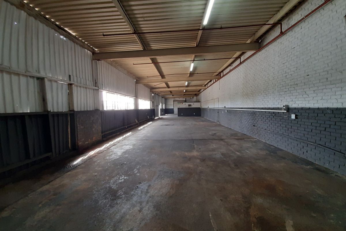 Spacious industrial utility area featuring exposed steel beams, corrugated metal walls, painted brickwork, and durable concrete flooring with fluorescent lighting.