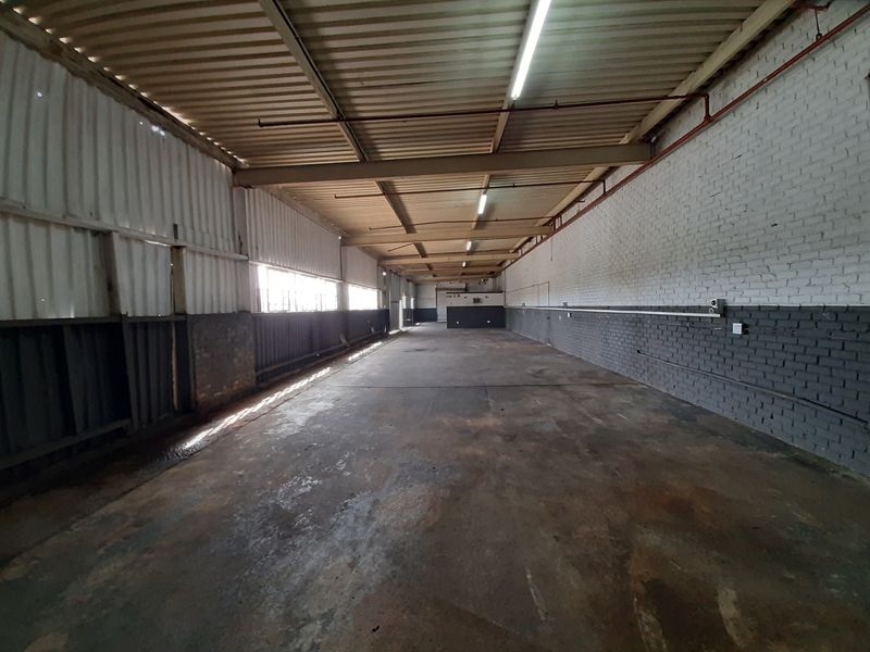 Spacious industrial utility area featuring exposed steel beams, corrugated metal walls, painted brickwork, and durable concrete flooring with fluorescent lighting.