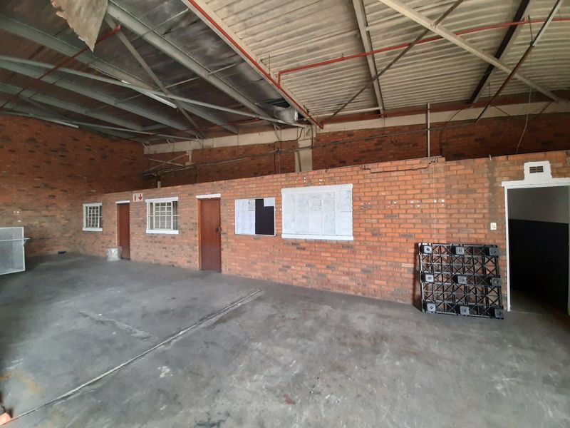 Spacious industrial utility area featuring exposed brick walls, high steel truss ceilings with fire sprinkler systems, and durable concrete flooring.
