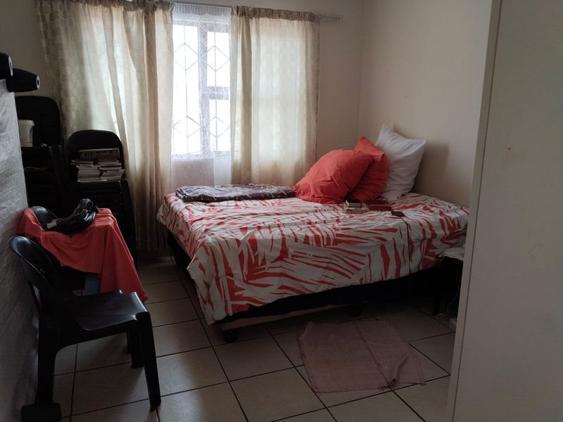 A standard bedroom featuring tiled flooring and security burglar bars on the window, providing a functional living space.