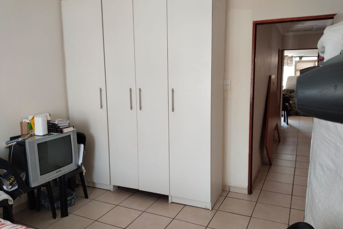 A bedroom featuring a large white built-in wardrobe and tiled flooring, with a doorway leading to an adjacent hallway.