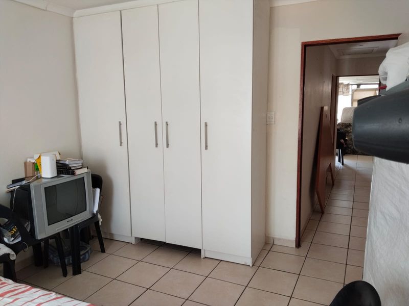 A bedroom featuring a large white built-in wardrobe and tiled flooring, with a doorway leading to an adjacent hallway.