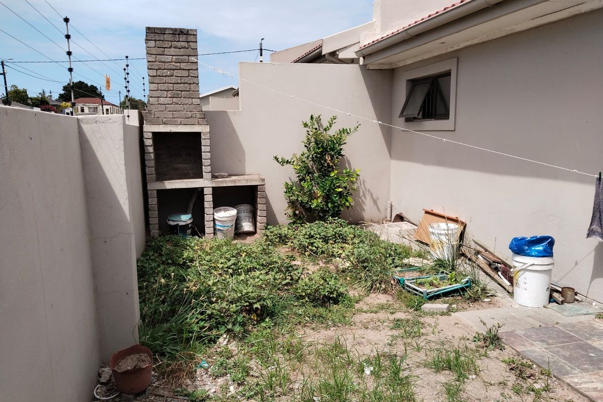 Rear courtyard area featuring a built-in brick braai and perimeter wall, currently requiring landscaping and maintenance to improve the outdoor space.