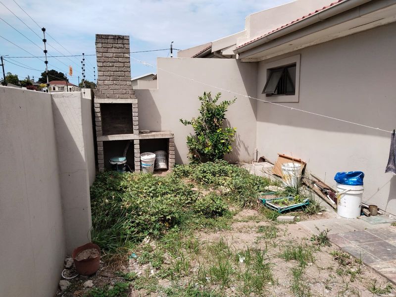 Rear courtyard area featuring a built-in brick braai and perimeter wall, currently requiring landscaping and maintenance to improve the outdoor space.