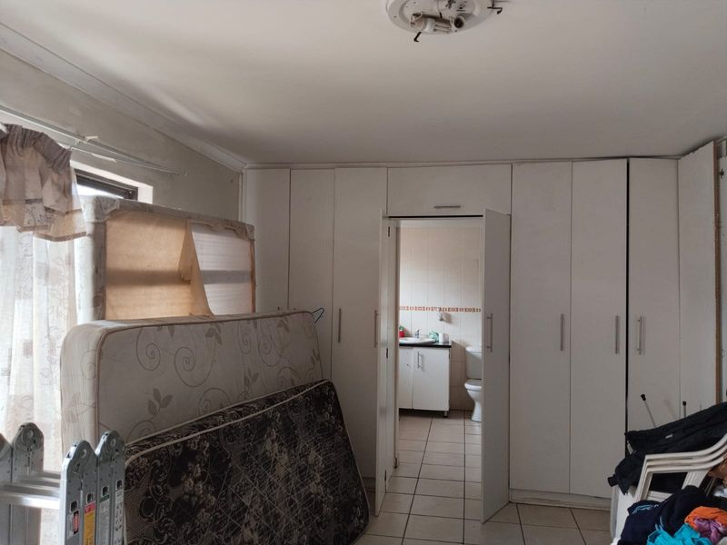 Bedroom featuring extensive built-in cupboards and tiled flooring, with direct access to an en-suite bathroom. Requires cosmetic updates and repairs.