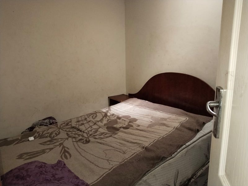 A compact bedroom featuring plain walls and a standard door entry, currently requiring cosmetic updates and fresh paint to improve the overall condition.